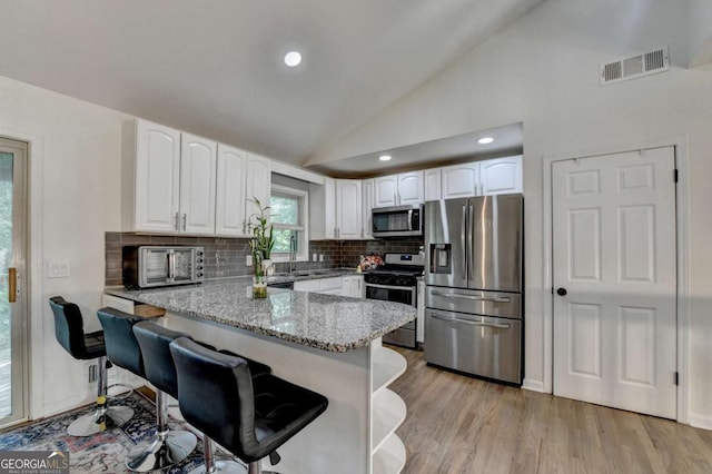 1358 Millstream Trl, Lawrenceville, GA 30044 - kitchen with stainless steel appliances, a peninsula, lofted ceiling, light stone counters, and white cabinetry