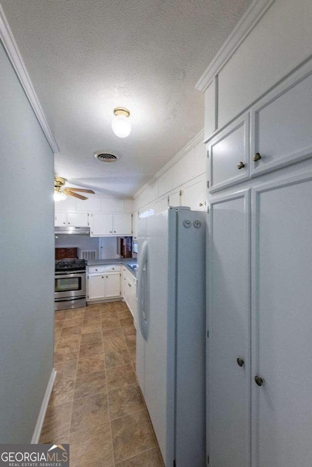 675 Mountain View Dr, Thomaston, GA 30286 - kitchen with freestanding refrigerator, stainless steel gas range, white cabinets, under cabinet range hood, and a ceiling fan
