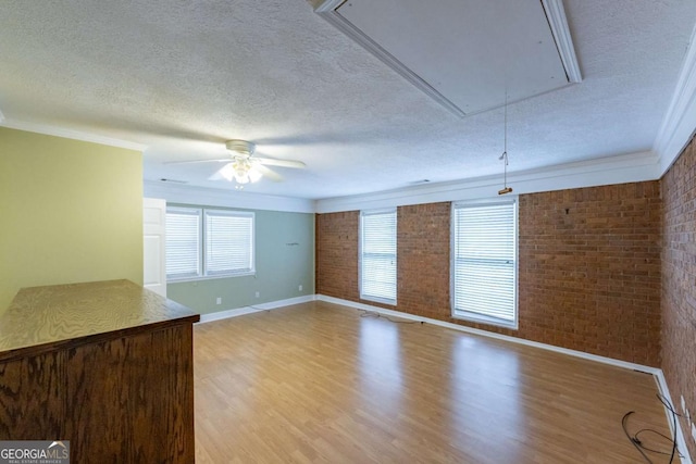 675 Mountain View Dr, Thomaston, GA 30286 - unfurnished living room with attic access, a textured ceiling, brick wall, light wood-style flooring, and crown molding