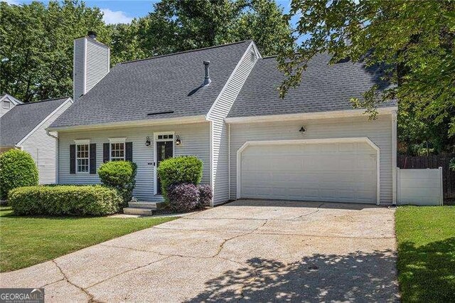 new england style home with concrete driveway, a garage, a chimney, a front lawn, and roof with shingles