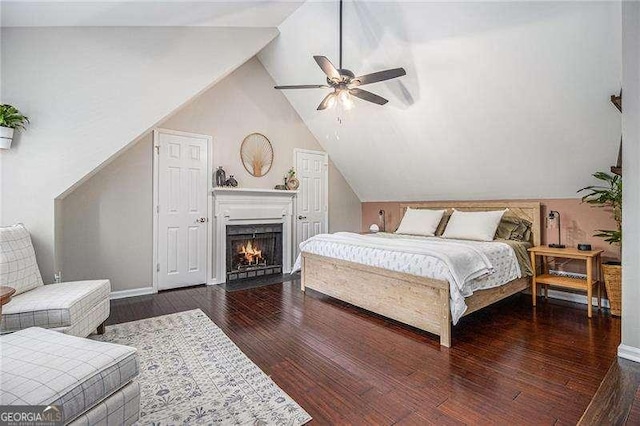 bedroom featuring wood finished floors, lofted ceiling, a fireplace with flush hearth, baseboards, and ceiling fan