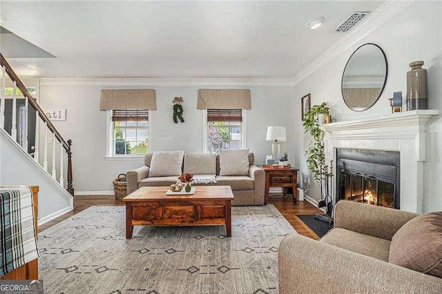 living room featuring healthy amount of natural light, stairs, a fireplace with flush hearth, baseboards, and ornamental molding