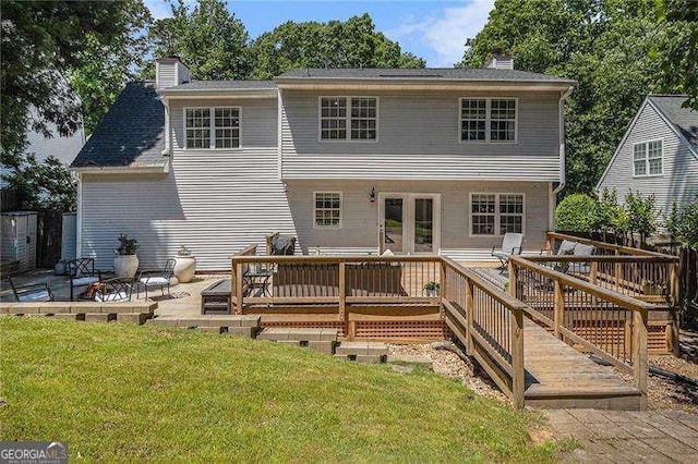 rear view of property with a chimney, a lawn, a deck, and a patio area