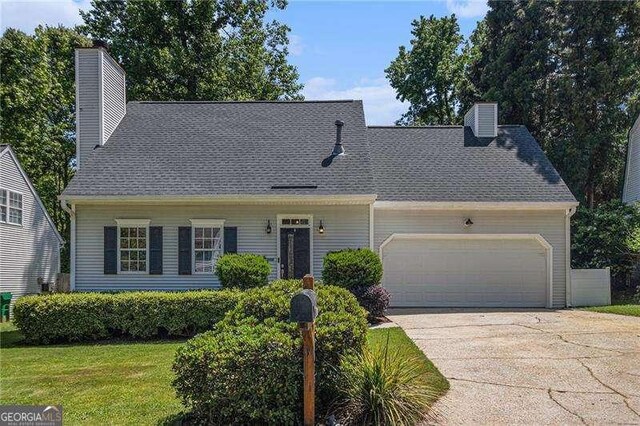 cape cod-style house featuring a chimney, a garage, concrete driveway, and a front yard