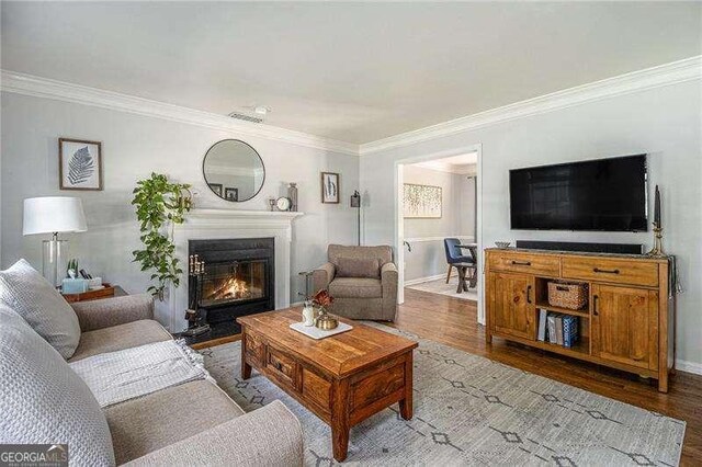 living room with wood finished floors, a glass covered fireplace, ornamental molding, and baseboards