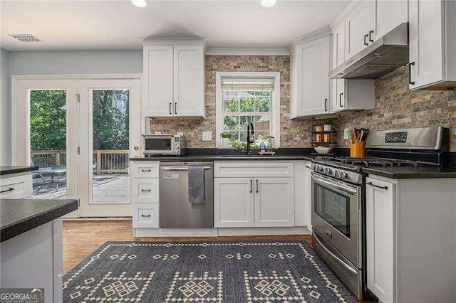 kitchen featuring stainless steel appliances, under cabinet range hood, a sink, dark countertops, and recessed lighting