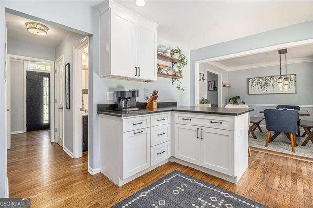 kitchen with dark countertops, light wood-type flooring, white cabinets, and a peninsula