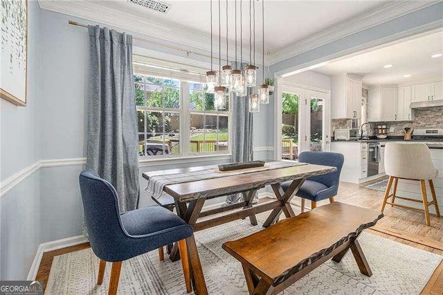 dining area featuring healthy amount of natural light, light wood finished floors, crown molding, and french doors