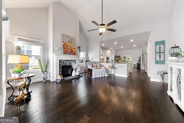 75 Georgian Oaks Ct, Newnan, GA 30265 - living area featuring a stone fireplace, a ceiling fan, dark wood-style floors, high vaulted ceiling, and baseboards