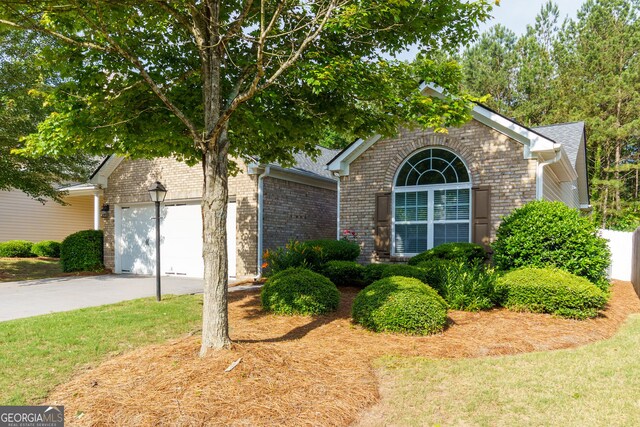 view of property hidden behind natural elements featuring driveway, brick siding, an attached garage, and a front lawn