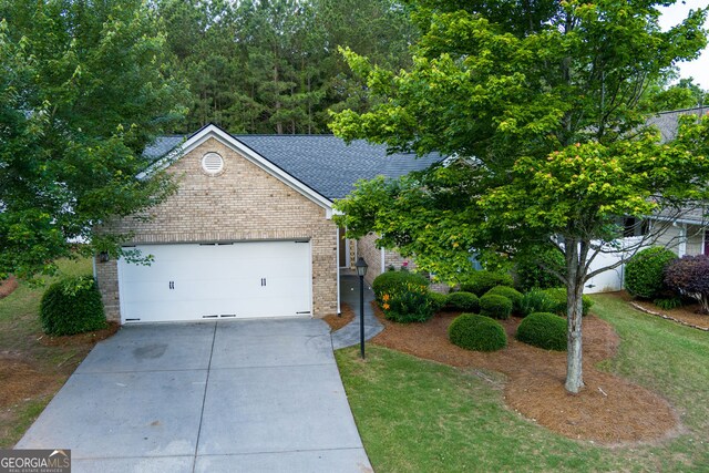 view of property hidden behind natural elements featuring brick siding, concrete driveway, a garage, and roof with shingles