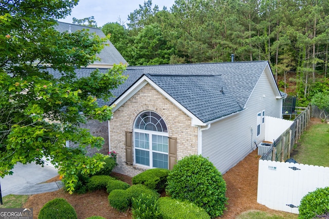 view of side of home with a shingled roof, central air condition unit, brick siding, and fence