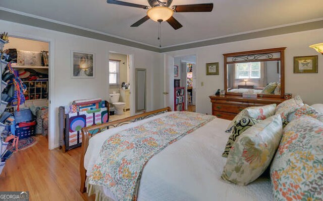 bedroom featuring a walk in closet, wood finished floors, multiple windows, a closet, and ornamental molding