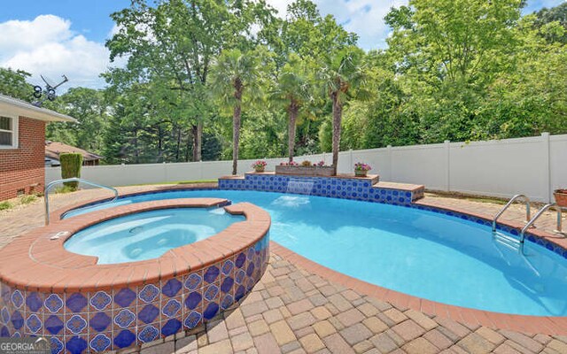 view of swimming pool with a fenced backyard, a pool with connected hot tub, and view of wooded area