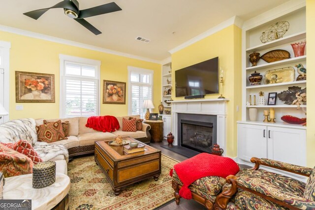 963 S On Main Dr, Woodstock, GA 30188 - living room featuring crown molding, a fireplace with flush hearth, built in features, a ceiling fan, and wood finished floors