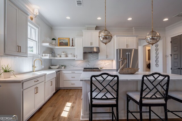 2970 Greenleffe Dr, Statham, GA 30666 - kitchen with appliances with stainless steel finishes, under cabinet range hood, a sink, white cabinets, and a kitchen breakfast bar