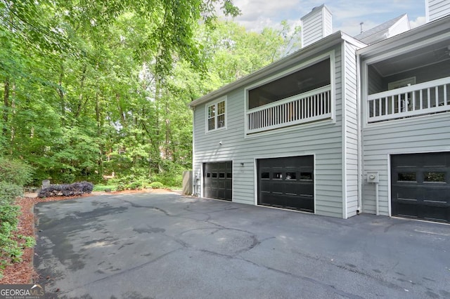 view of home's exterior featuring an attached garage, a chimney, and driveway