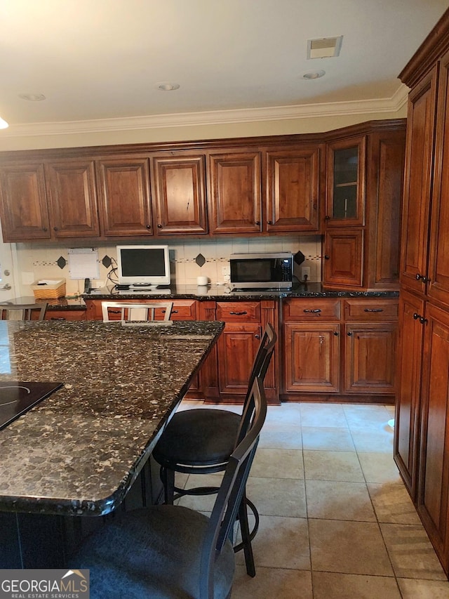 213 Falcon Crst, Warner Robins, GA 31088 - kitchen featuring stainless steel microwave, dark stone countertops, ornamental molding, a kitchen breakfast bar, and tasteful backsplash