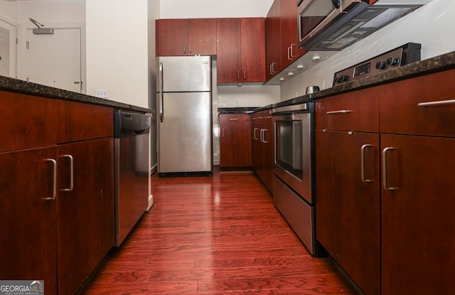kitchen with stainless steel appliances, dark wood-type flooring, and dark stone counters