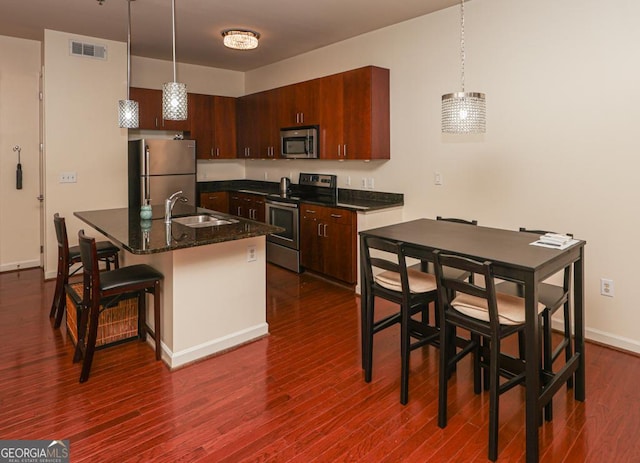 kitchen featuring stainless steel appliances, a sink, dark wood-style flooring, decorative light fixtures, and a kitchen island with sink