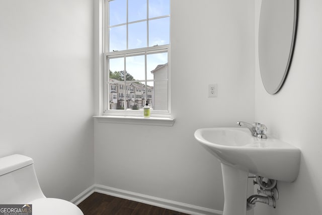 half bathroom featuring baseboards, wood finished floors, and toilet