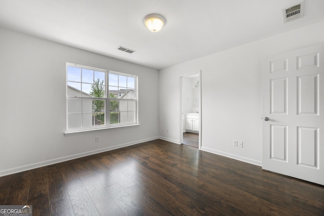 unfurnished bedroom featuring dark wood-type flooring, baseboards, and connected bathroom