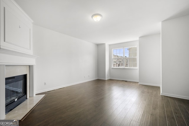 unfurnished living room featuring a fireplace with flush hearth, dark wood finished floors, and baseboards
