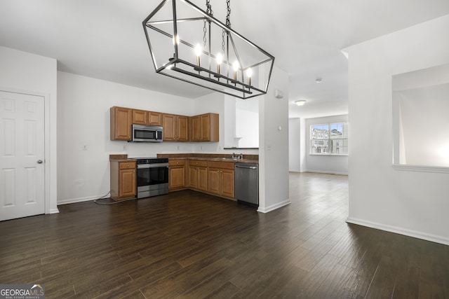 kitchen featuring appliances with stainless steel finishes, a sink, dark wood-type flooring, brown cabinetry, and baseboards
