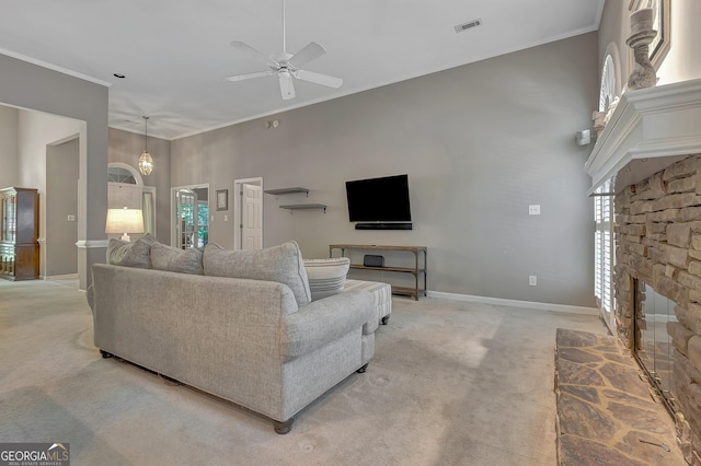 living area with a stone fireplace, light colored carpet, ceiling fan, baseboards, and ornamental molding