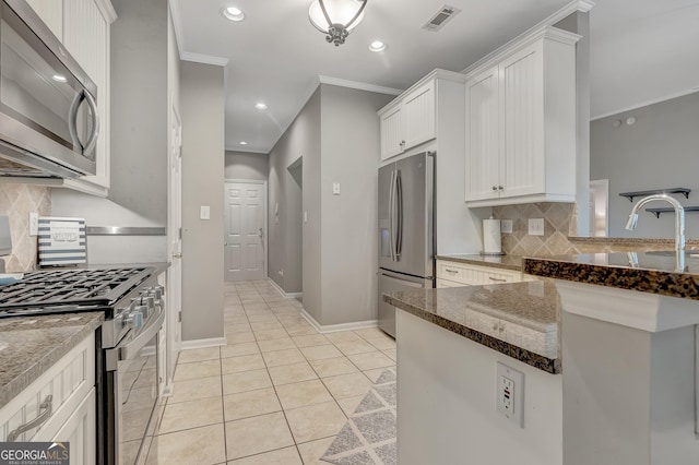 kitchen with appliances with stainless steel finishes, backsplash, white cabinets, dark stone counters, and crown molding