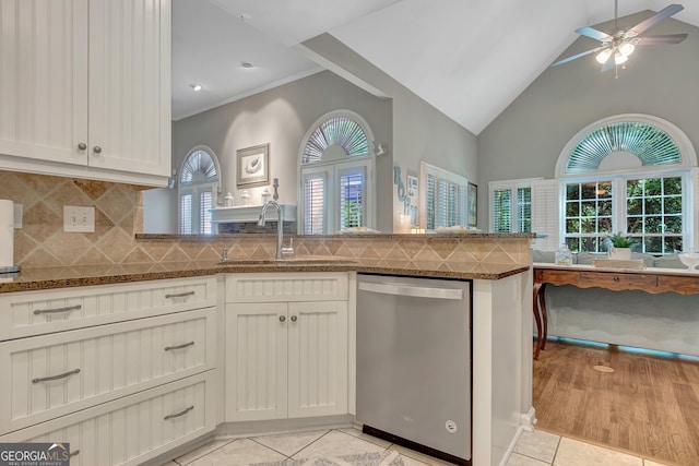 kitchen featuring stainless steel dishwasher, a sink, dark stone countertops, light tile patterned flooring, and a peninsula