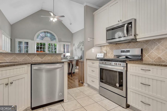 kitchen featuring stainless steel appliances, decorative backsplash, ceiling fan, dark stone countertops, and high vaulted ceiling