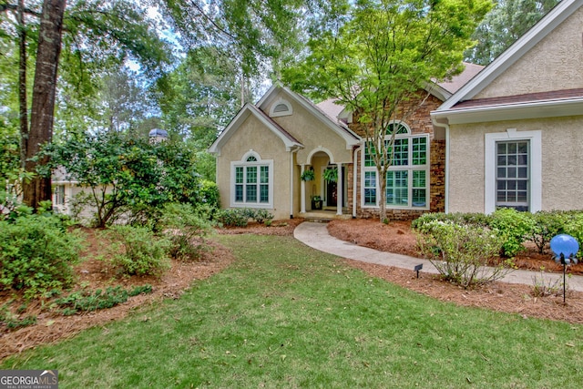 traditional-style home with stucco siding, a front yard, and stone siding