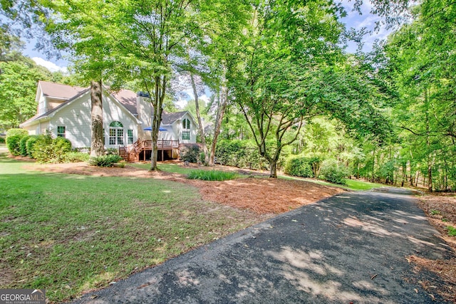 view of front facade featuring a wooden deck, a chimney, a front yard, and asphalt driveway