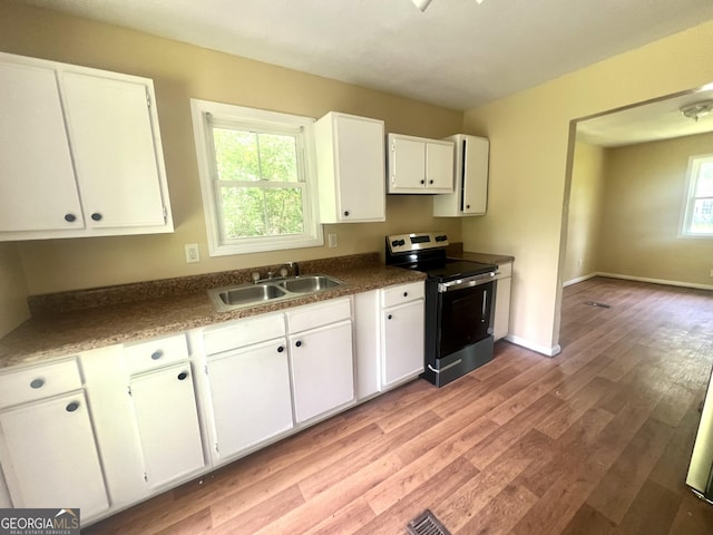 kitchen with electric range, a sink, light wood-style floors, white cabinetry, and dark countertops