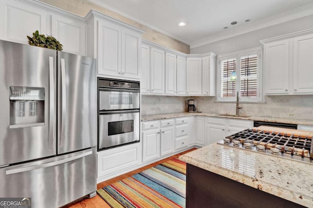 kitchen with stainless steel appliances, a sink, ornamental molding, light wood-type flooring, and white cabinets