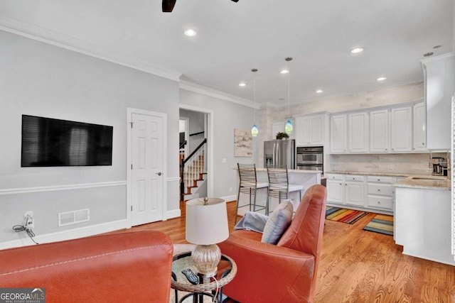 living room featuring light wood-style flooring, recessed lighting, a ceiling fan, ornamental molding, and stairs