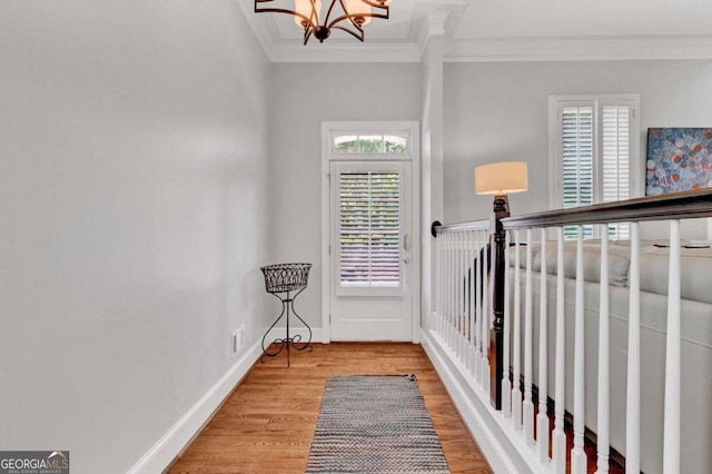 corridor featuring crown molding, wood finished floors, a chandelier, and baseboards