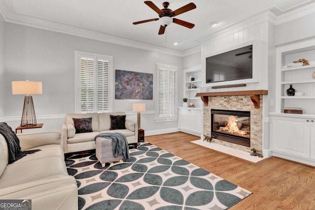 living room with a ceiling fan, light wood finished floors, ornamental molding, built in features, and a fireplace