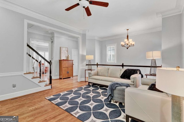 living area with a ceiling fan, wood finished floors, a chandelier, crown molding, and stairway