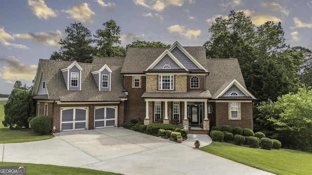 view of front of house with a porch, driveway, a front lawn, brick siding, and an attached garage
