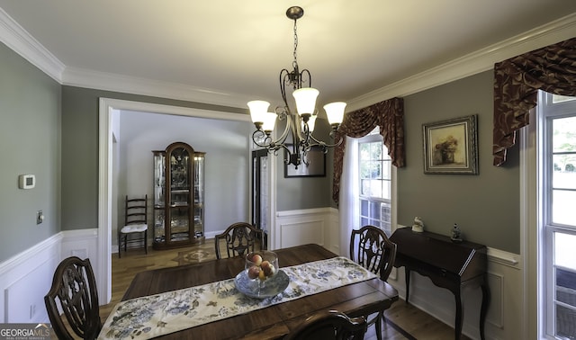 dining space featuring wainscoting, a chandelier, ornamental molding, plenty of natural light, and wood finished floors