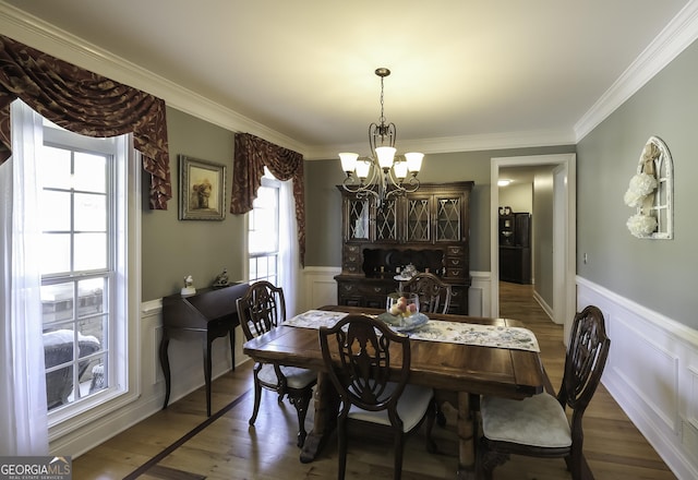 dining area featuring a chandelier, a wainscoted wall, a decorative wall, dark wood finished floors, and ornamental molding