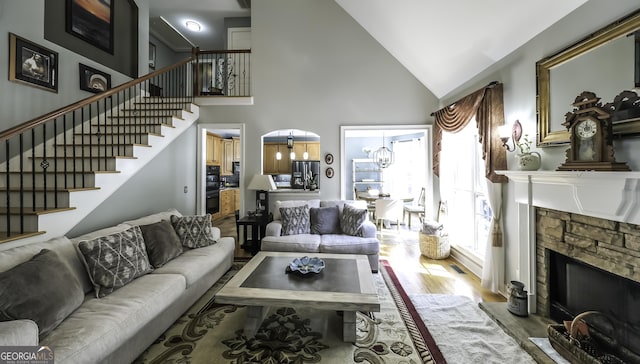 living room with a chandelier, a fireplace, stairs, wood finished floors, and high vaulted ceiling