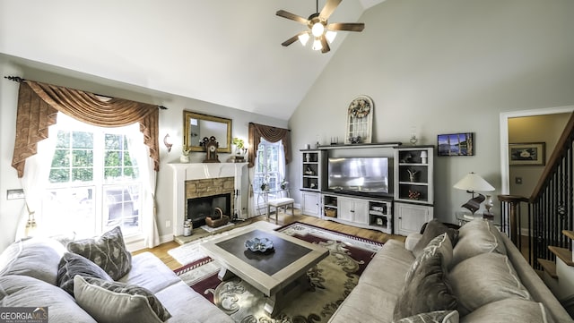 living area featuring a ceiling fan, high vaulted ceiling, a fireplace, wood finished floors, and stairs