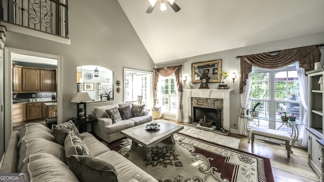 living area with high vaulted ceiling, plenty of natural light, ceiling fan, a fireplace, and light wood-style floors