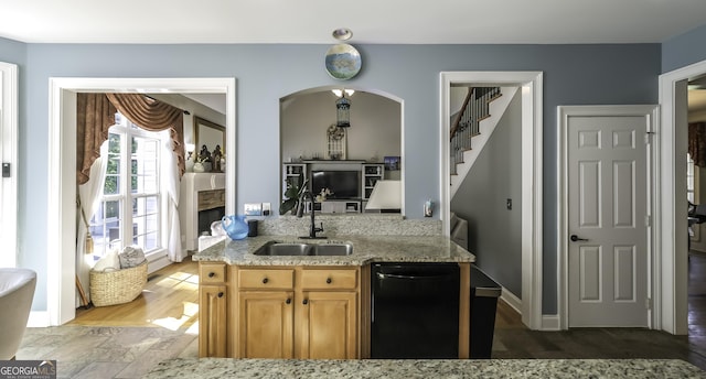 kitchen with a sink, dishwasher, light stone counters, light brown cabinetry, and arched walkways