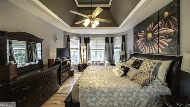 bedroom featuring a raised ceiling, light wood-style floors, ceiling fan, and ornamental molding