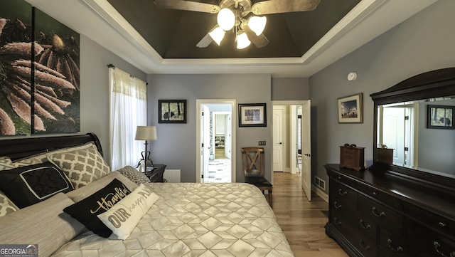 bedroom with a tray ceiling, wood finished floors, and ceiling fan