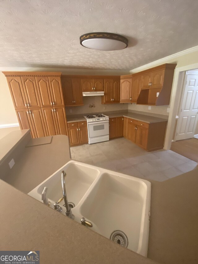 1669 Azalea Dr, Lawrenceville, GA 30043 - kitchen with white range with gas stovetop, under cabinet range hood, brown cabinetry, a sink, and a textured ceiling